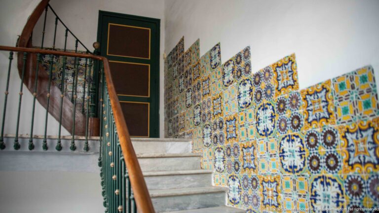 Marble stairs beside a green balustrade and a wall covered with colorful floral and geometric ceramic tiles.