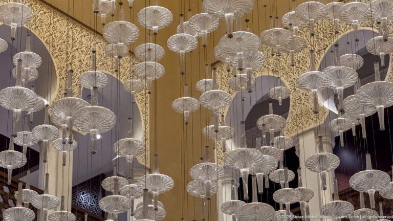 Many suspended glass lamps hanging at different heights beneath ornate arches and a warm-toned ceiling.