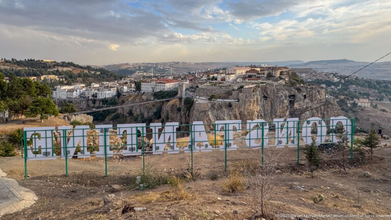 Large Constantine sign in the foreground with the city, cliffs, roads, and gorge spread across the background.