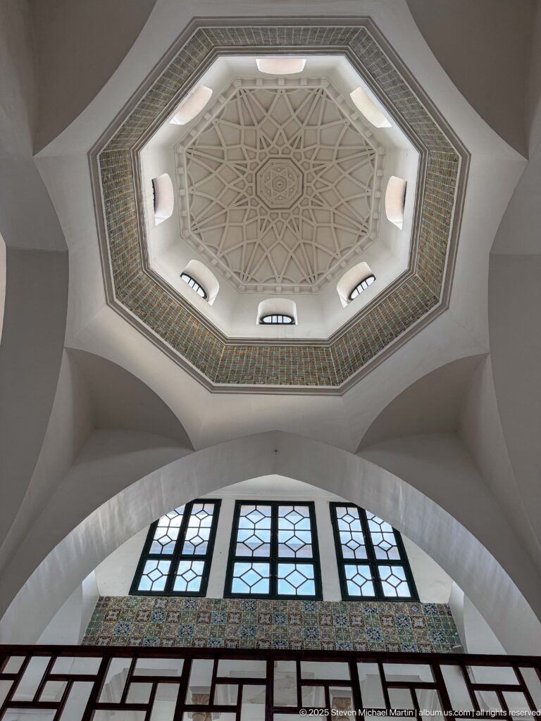 Octagonal geometric ceiling with small high windows above an arched window wall and dark gallery railing.