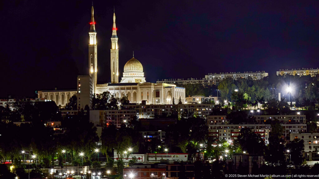Illuminated Emir Abdelkader Mosque at night with a large central dome and twin minarets above Constantine’s city lights.