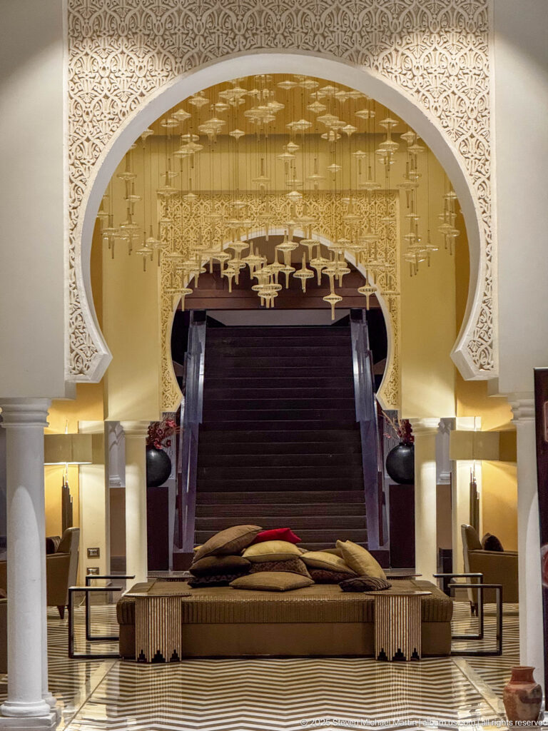 Lounge seating beneath a carved white horseshoe arch with suspended glass lights, columns, and patterned flooring.