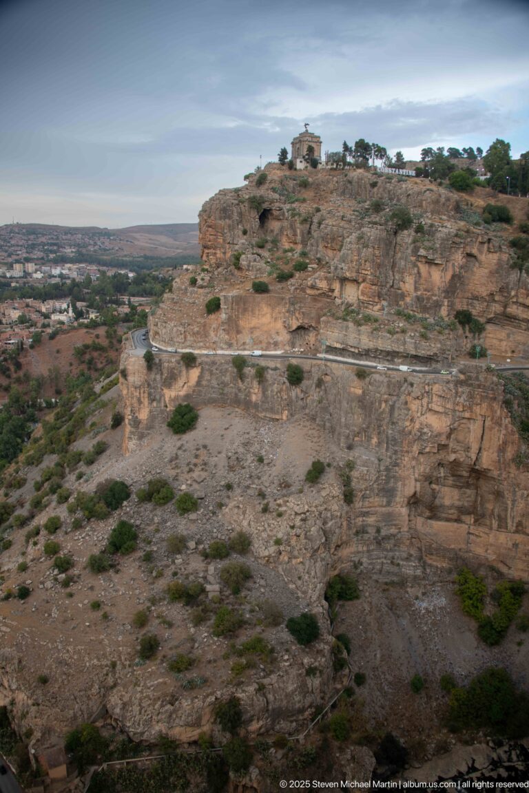 Rocky plateau with sparse shrubs and a small hilltop structure above Constantine’s gorge.