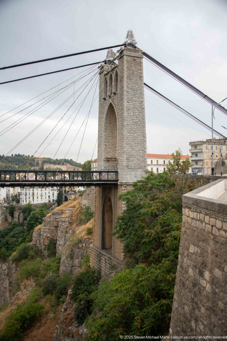 Stone tower of Sidi M’Cid Bridge with pointed arch, paired openings, suspension cables, and bridge deck.