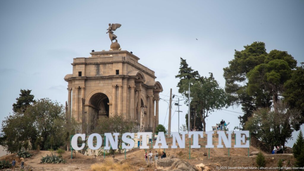 Monument aux Morts above large white CONSTANTINE letters on a rocky hill with scattered visitors.
