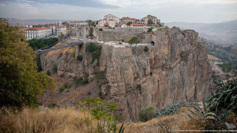 Wide view of Sidi M’Cid Bridge crossing a sheer gorge below cliff-top buildings and distant highlands.