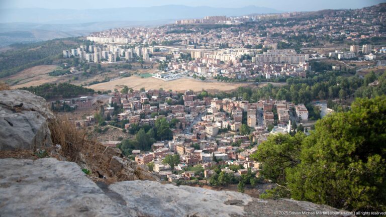 Elevated panorama over Constantine’s neighborhoods, apartment blocks, green corridors, and distant highland ridges.
