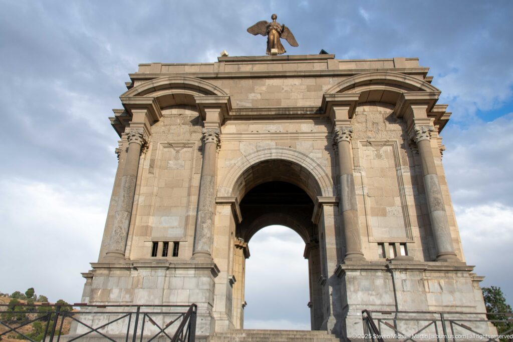 Low-angle frontal view of Constantine’s Monument aux Morts, with paired columns, central arch, and winged figure above.