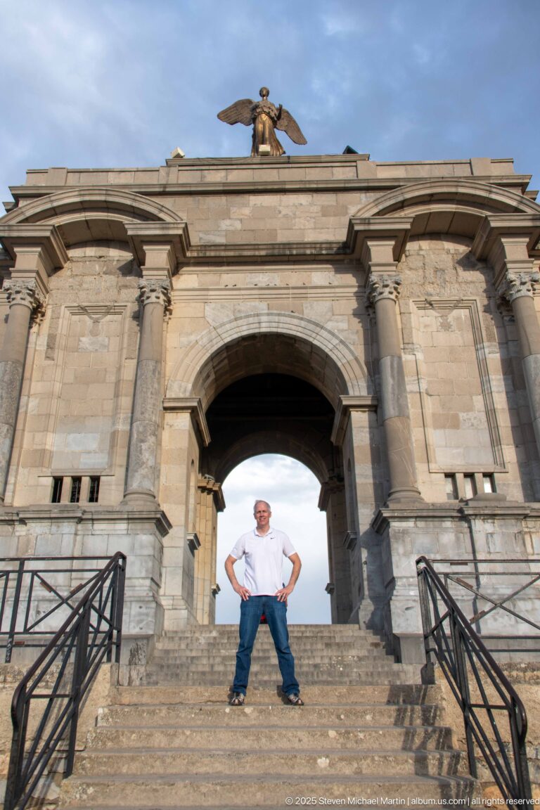 Man standing on the steps beneath the central arch of Constantine’s Monument aux Morts.