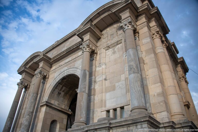 Oblique low-angle view of stone columns, capitals, cornices, and central arch on Constantine’s Monument aux Morts.