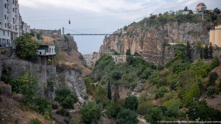 Green ravine between Constantine’s cliffs, with a distant suspension bridge and Monument aux Morts on the far rim.