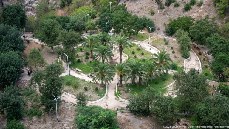 Terraced garden with curving paths, palms, trees, and light poles on a steep Constantine slope.