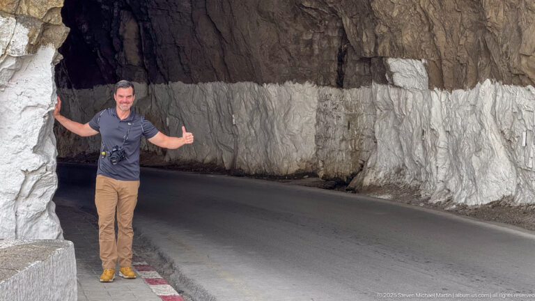 Man beside a curving road tunnel cut through rough rock with whitewashed lower walls in Constantine.
