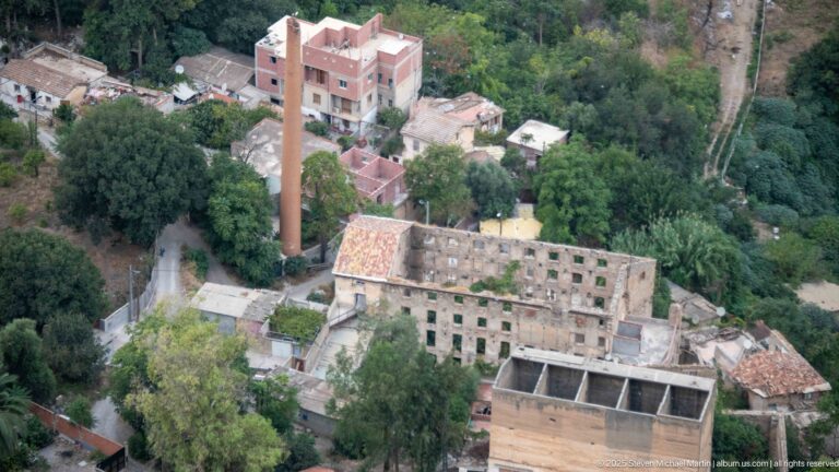 Stone building complex among trees with a tall narrow chimney or stack in Constantine’s ravine.