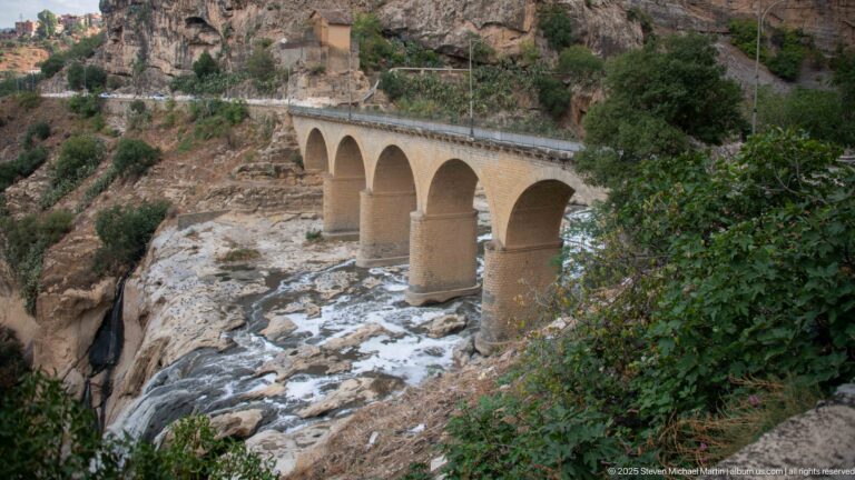 Four-arch masonry road bridge over pale bedrock and flowing water in Constantine’s gorge.