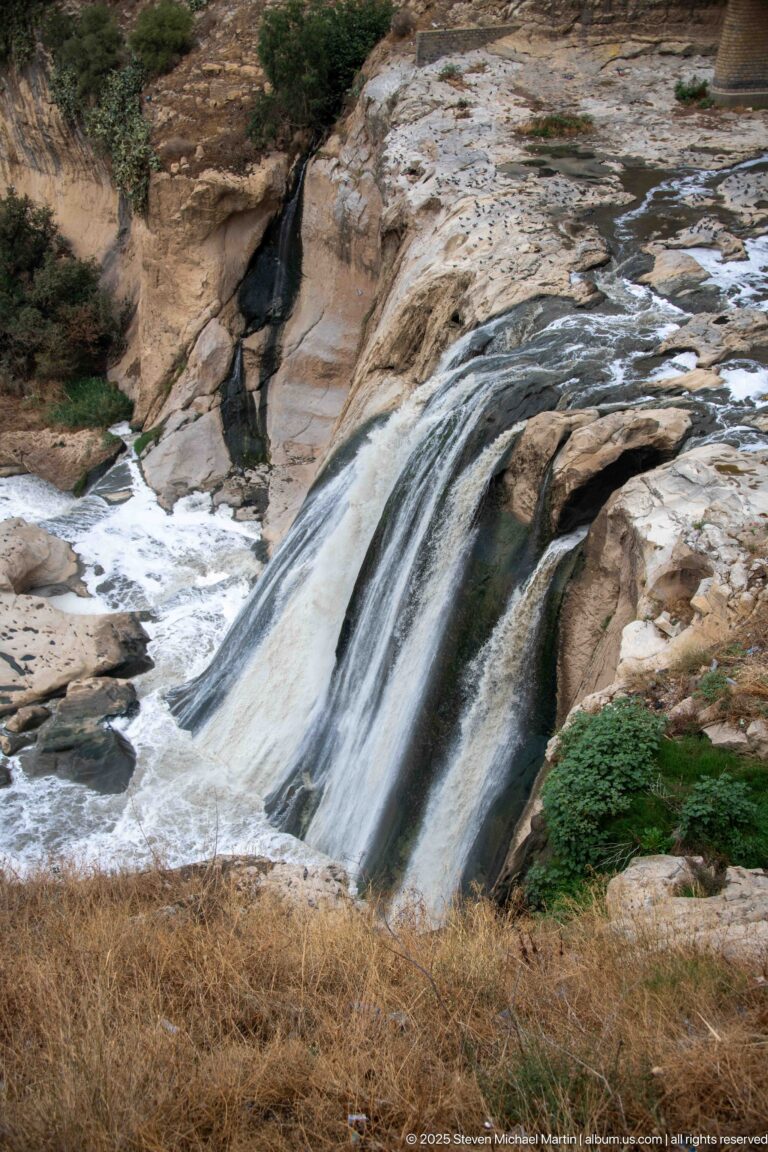Rhumel River spilling in a broad white cascade over smooth pale rock, with vegetation along the gorge edge.