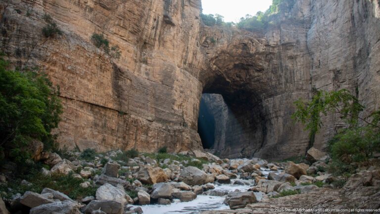 Large natural arch in layered cliff above a boulder-filled Rhumel River channel in Constantine’s gorge.