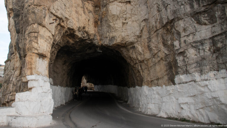 Curving road through a rough rock-cut tunnel with white-painted lower walls in Constantine.