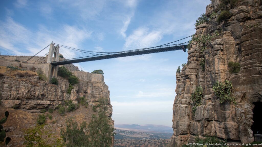 High suspension bridge with masonry tower spanning Constantine’s sheer gorge above a distant valley.