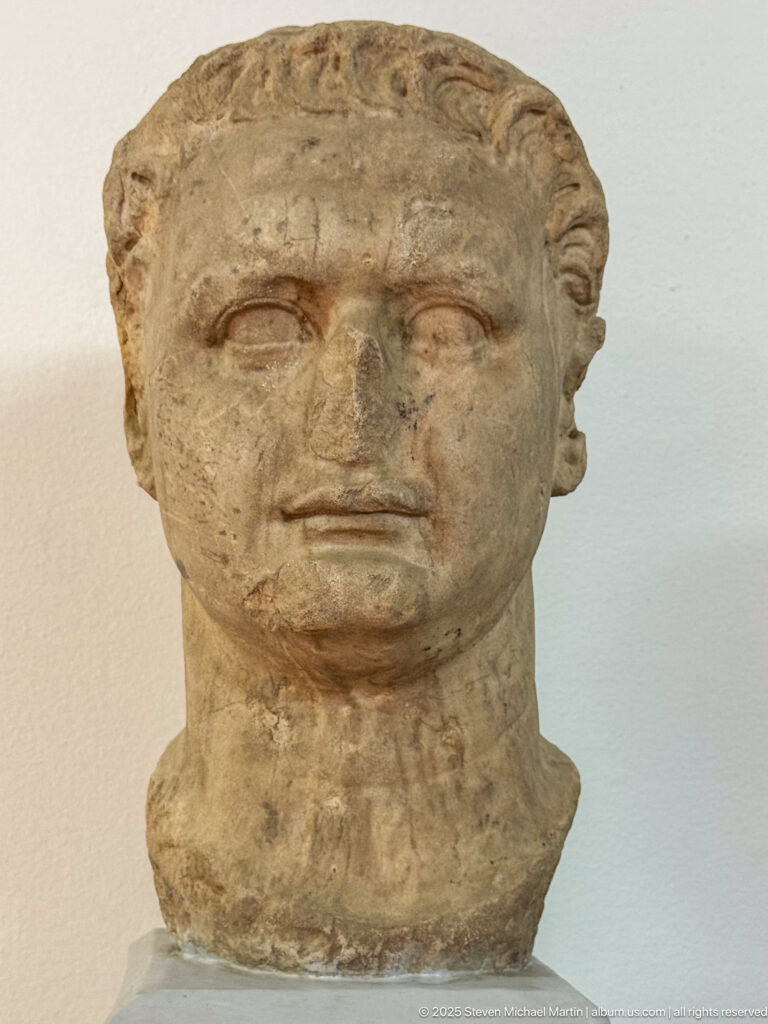 Weathered stone male portrait head with short hair, worn facial features, and a surviving neck.