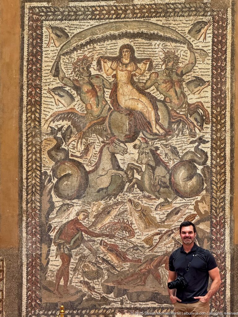 Visitor standing beside the large early-4th-century Triumph of Venus mosaic from Khenchela, displayed at the Cirta Museum.