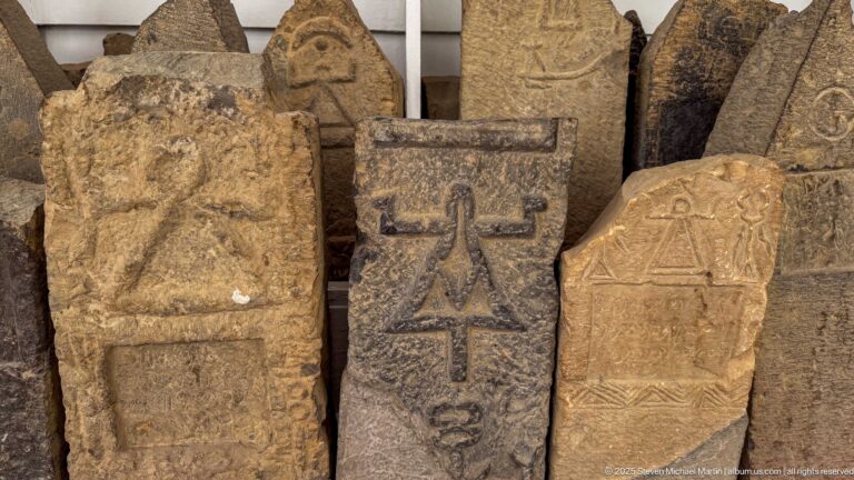 Cluster of small carved stone stelae with incised symbols, framed reliefs, and varied shapes.