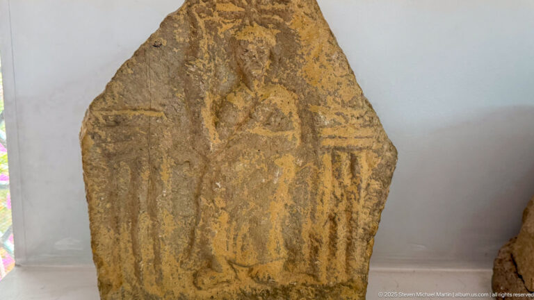 Weathered upright stone stele with a tapering top and shallow triangular and vertical carved motifs.