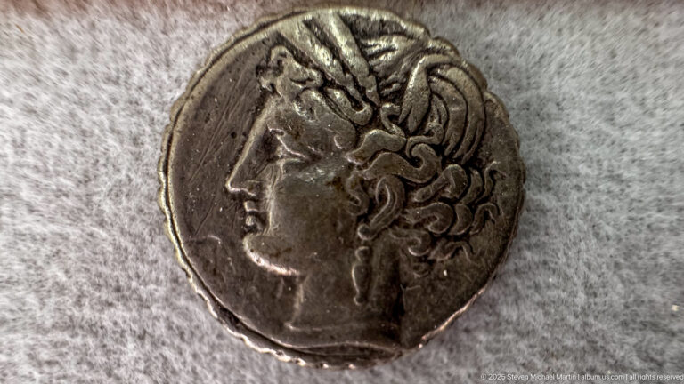 Close-up of an ancient silver coin with a left-facing female portrait and elaborate hair or headdress.