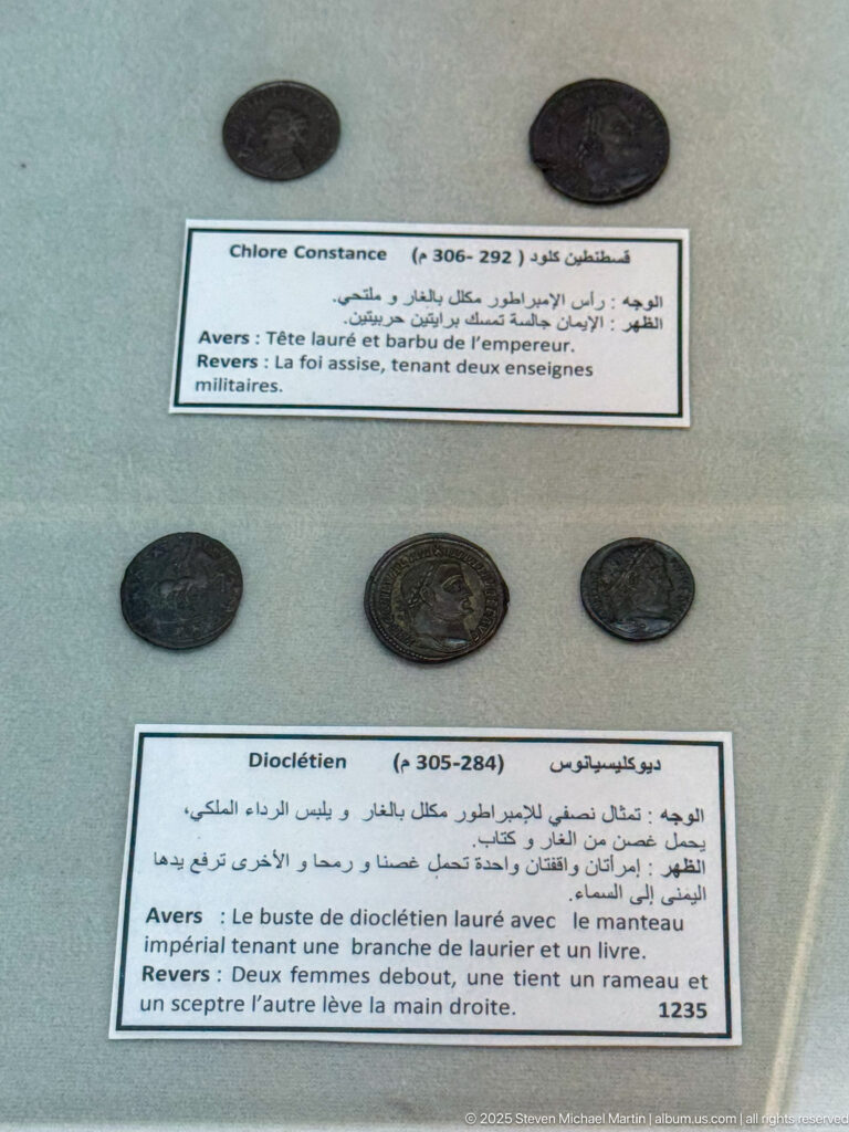 Ancient coins displayed beside bilingual labels naming Constantine I and Diocletian in a museum case.