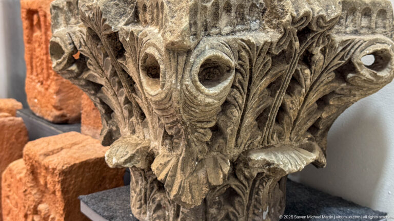 Close-up of a weathered carved stone capital with acanthus leaves, volutes, and deep drilled recesses.