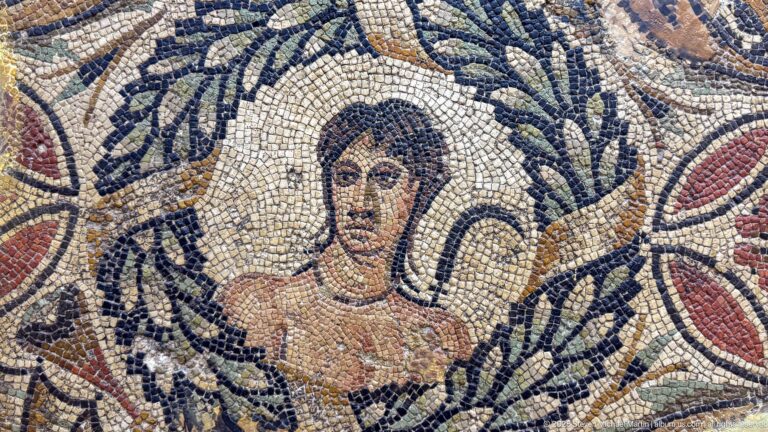 Close-up of a dark-haired female mosaic portrait wearing a necklace and framed by a leafy wreath.
