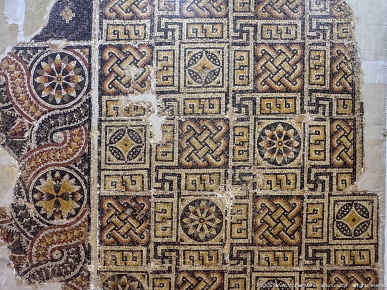 Geometric mosaic fragment with interlaced knots, rosettes, diamonds, and a contrasting patterned border.