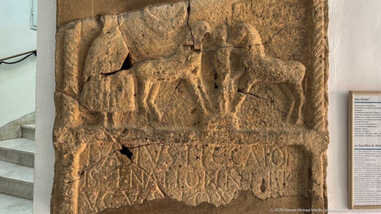 Weathered stone slab with a standing relief figure above a partially preserved carved inscription.