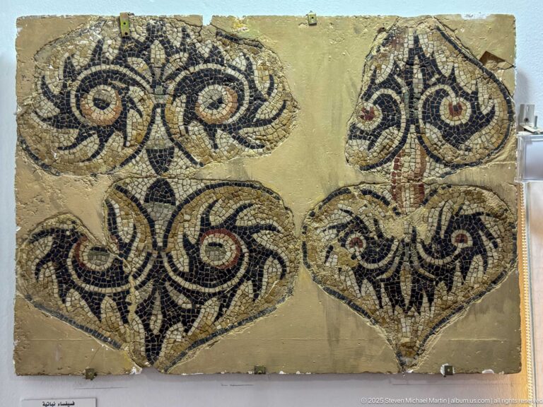 Ancient mosaic panel with four large heart-shaped foliate medallions in black, cream, and red tesserae.