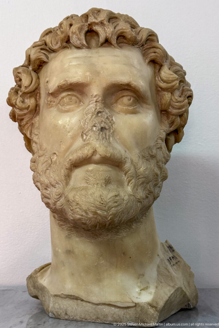 Marble portrait head of a mature man with curled hair, full beard, and a broken lower edge.