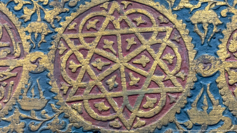 Close-up of a blue, burgundy, and gold decorative panel with an interlocking geometric rosette.