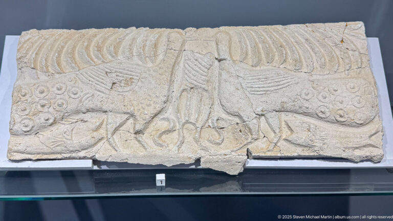 Rectangular carved stone relief with two opposing birds, a central vertical motif, and ornamental bands.