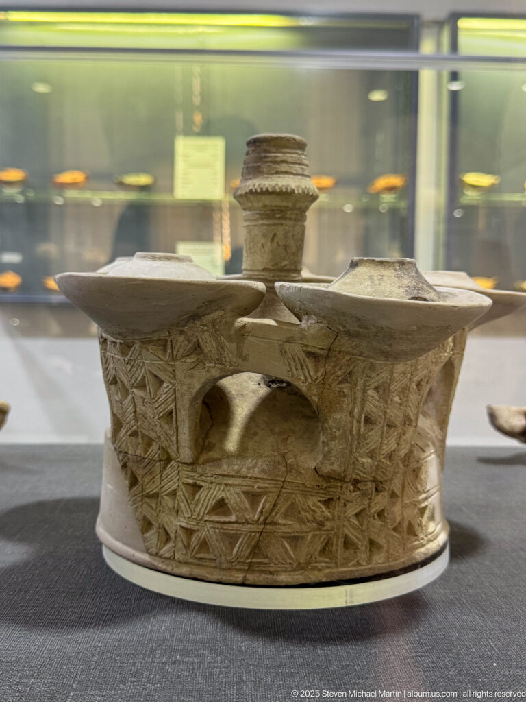 Complex ceramic vessel with two side chambers, a tall central neck, incised geometric decoration, and an arched opening.