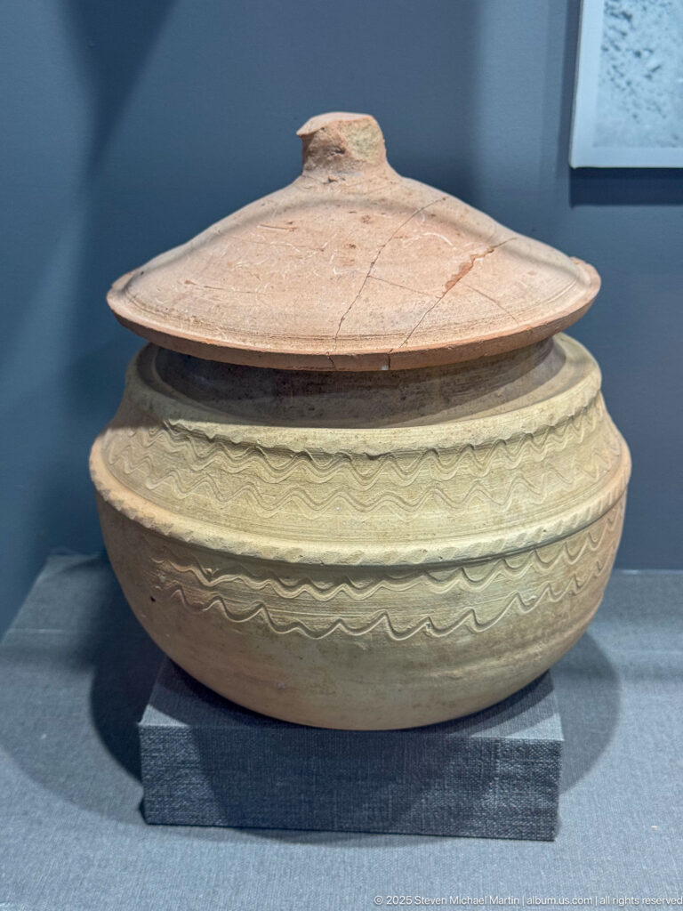 Wide rounded ceramic pot with a conical lid, central knob, and repeated wavy-line decoration.