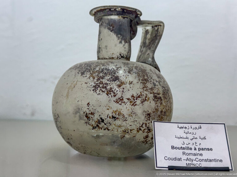 Weathered Roman glass bottle with rounded body, narrow neck, and small applied handle.