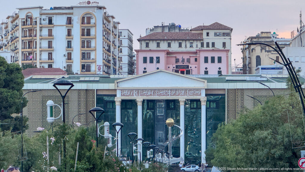 Front entrance of the Constantine Cirta Museum seen across a landscaped urban approach with taller buildings behind.
