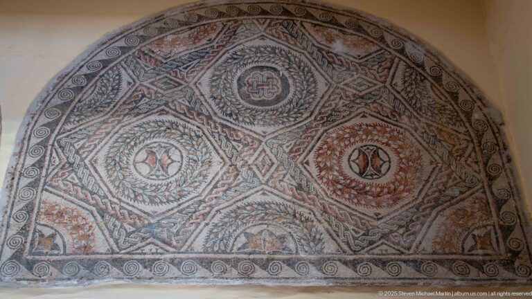 Semicircular Roman mosaic with circular medallions, diamond compartments, braided borders, and red, black, cream, and green tesserae.