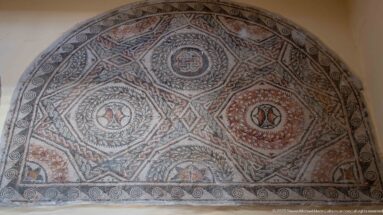 Semicircular Roman mosaic with circular medallions, diamond compartments, braided borders, and red, black, cream, and green tesserae.