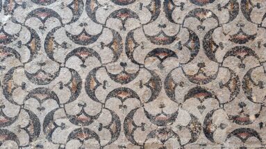 Close-up of a Roman mosaic with repeating cream fan-shaped motifs outlined in black and accented with red tesserae.