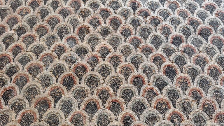 Close Roman mosaic detail of overlapping cream scallops outlined in black with red-brown centers.
