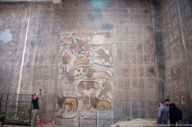 Great Hunt Mosaic from the House of Bacchus mounted on a tall museum wall, with visitors standing below.