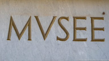 Close-up of the word MVSEE in large gold-toned serif letters set into a pale stone wall.