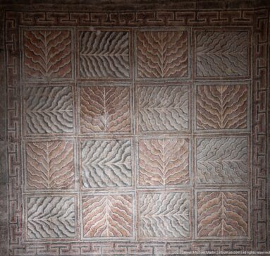 Rectangular Roman mosaic divided into square panels containing alternating leaf-like chevrons, framed by a dark meander border.