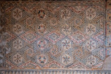 Polychrome Roman mosaic with three-dimensional cube patterns, rosettes, floral motifs, and red, cream, dark, and green tesserae.