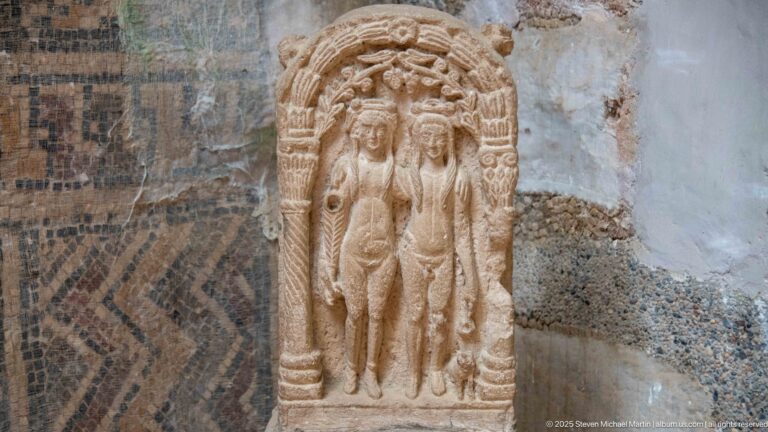 Stone relief of the Three Graces, three nude women standing together beneath a rounded carved frame.
